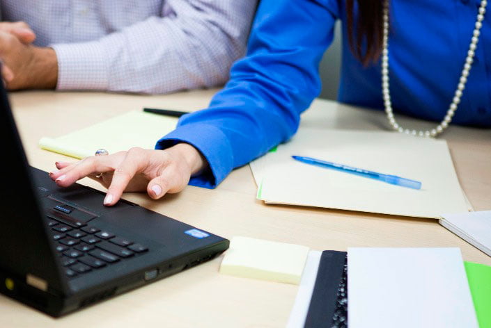 People's arms on desk with papers and laptop